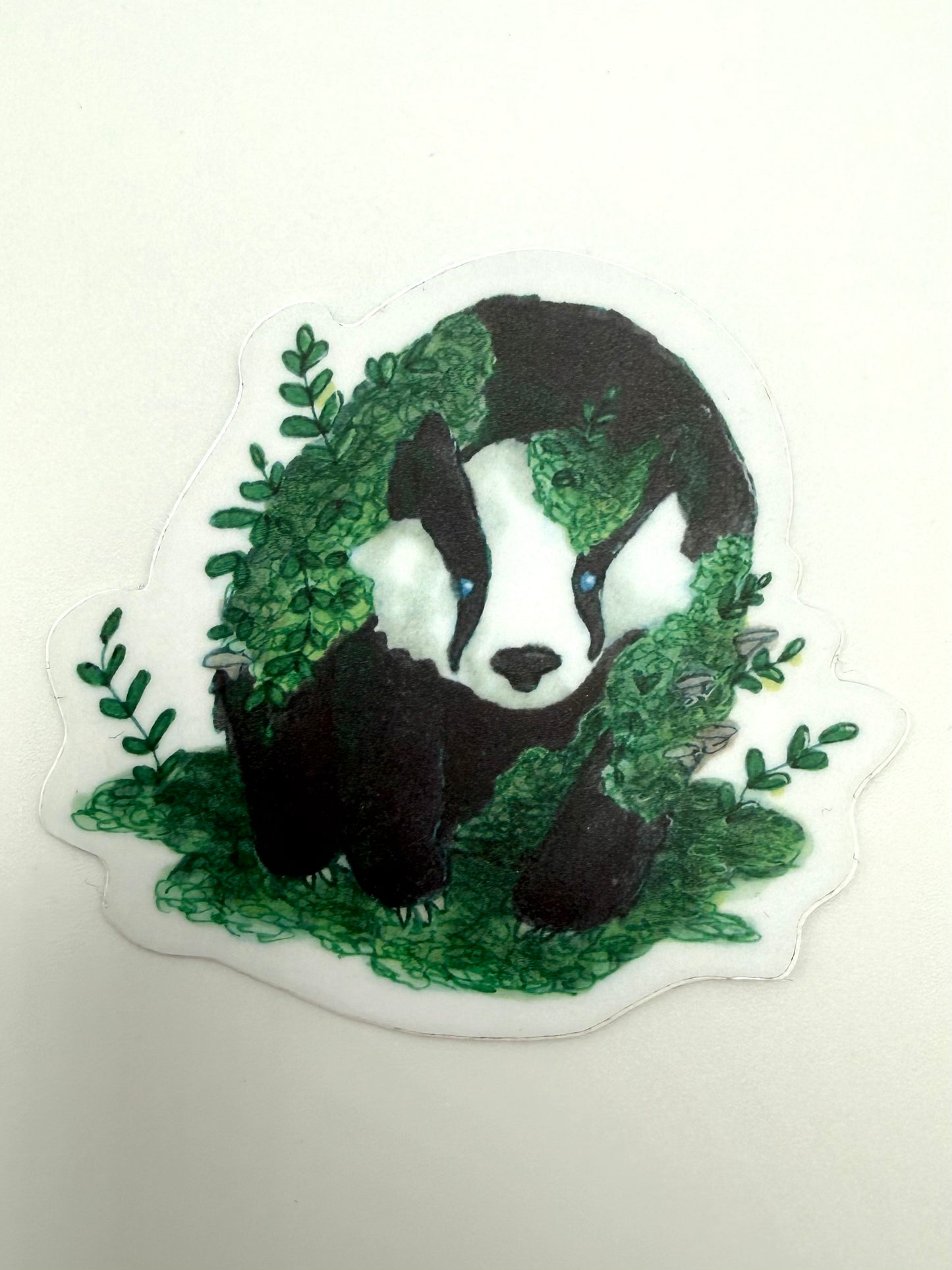 Sticker of a badger surrounded by green leaves on a white background