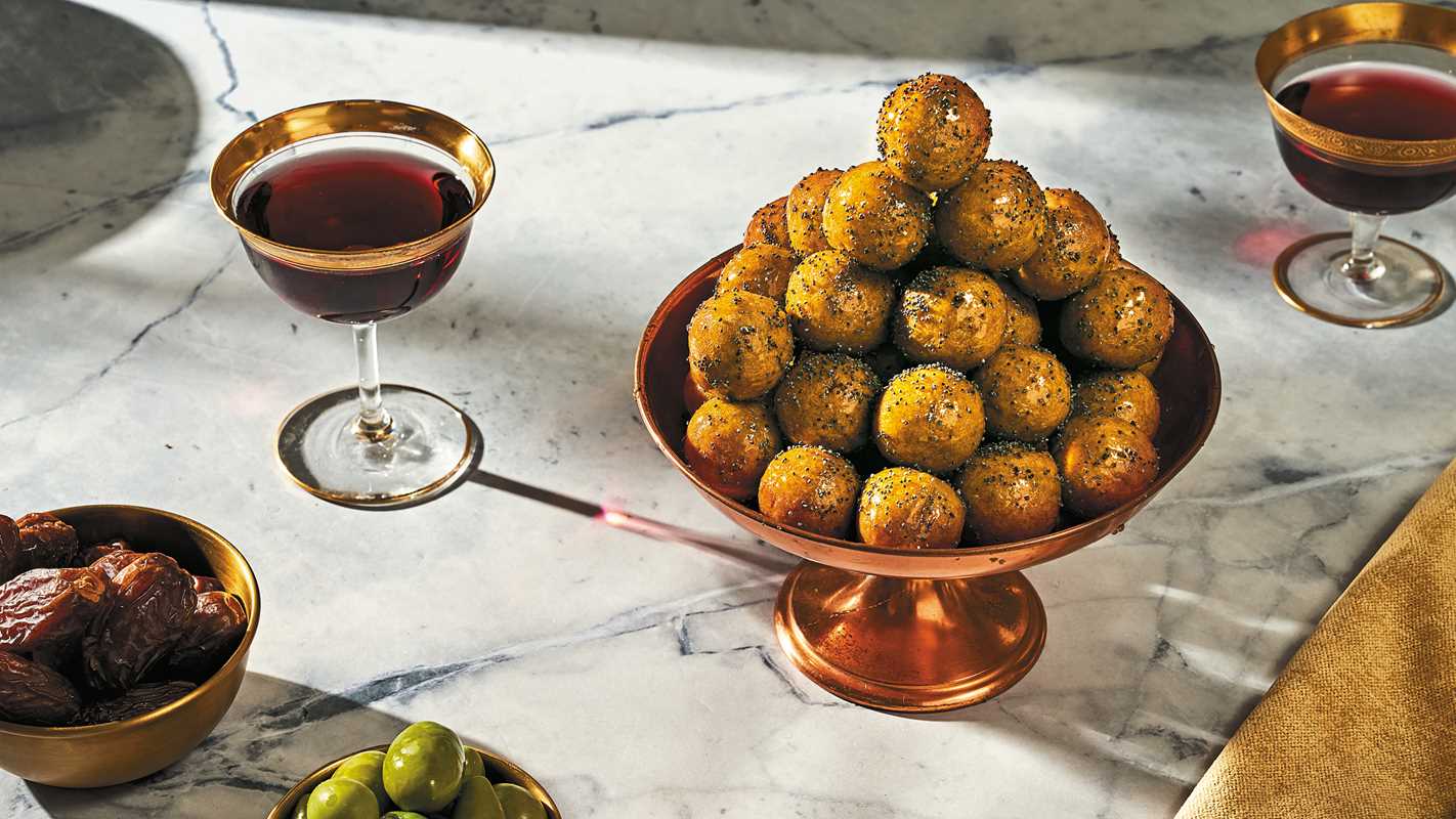 Culinary display with fried balls on a bronze stand, accompanied by glasses of red wine and dates on a marble surface.