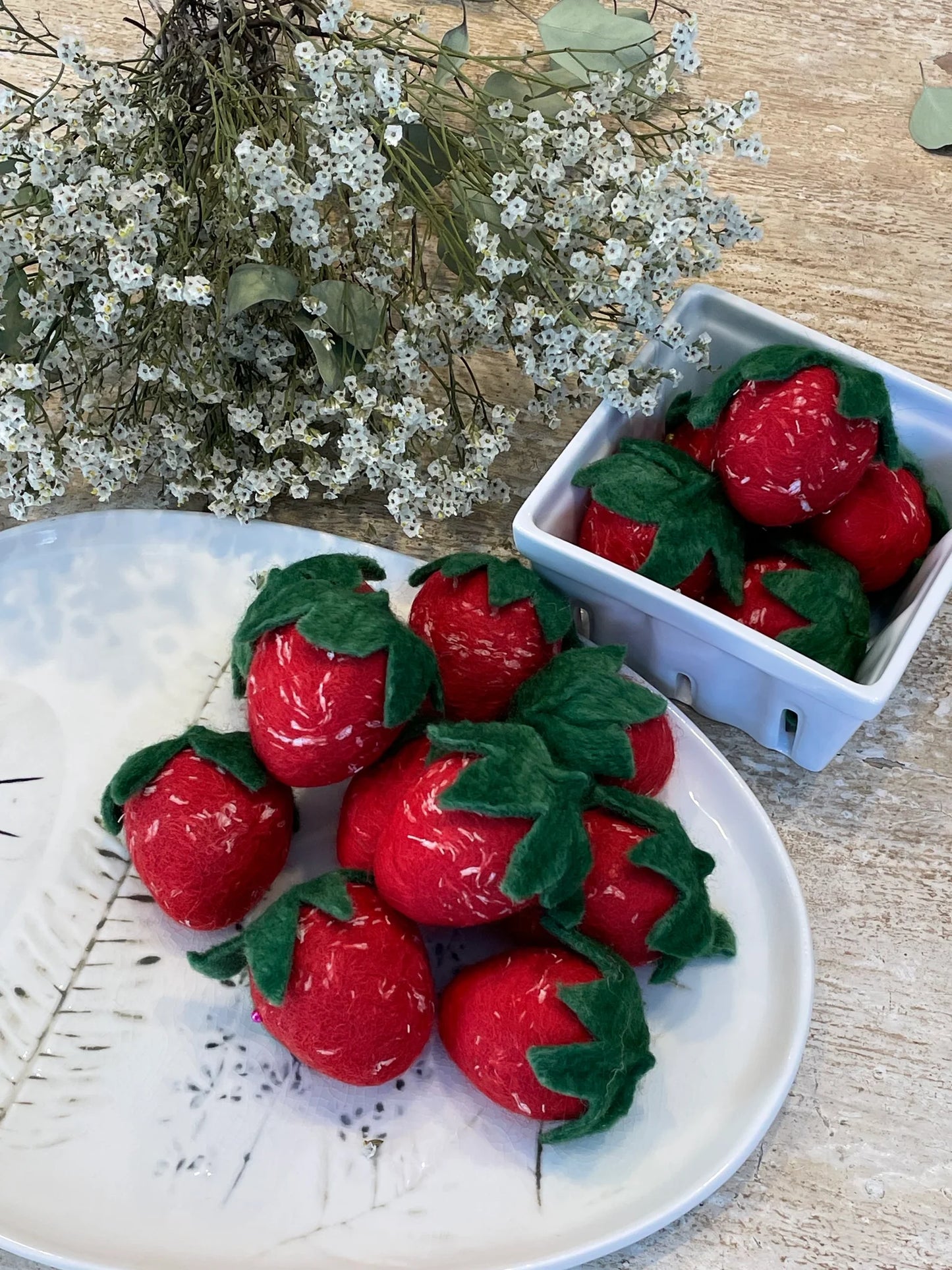 Red strawberry-shaped soaps on a white plate with a small container of soaps and white flowers in the background.