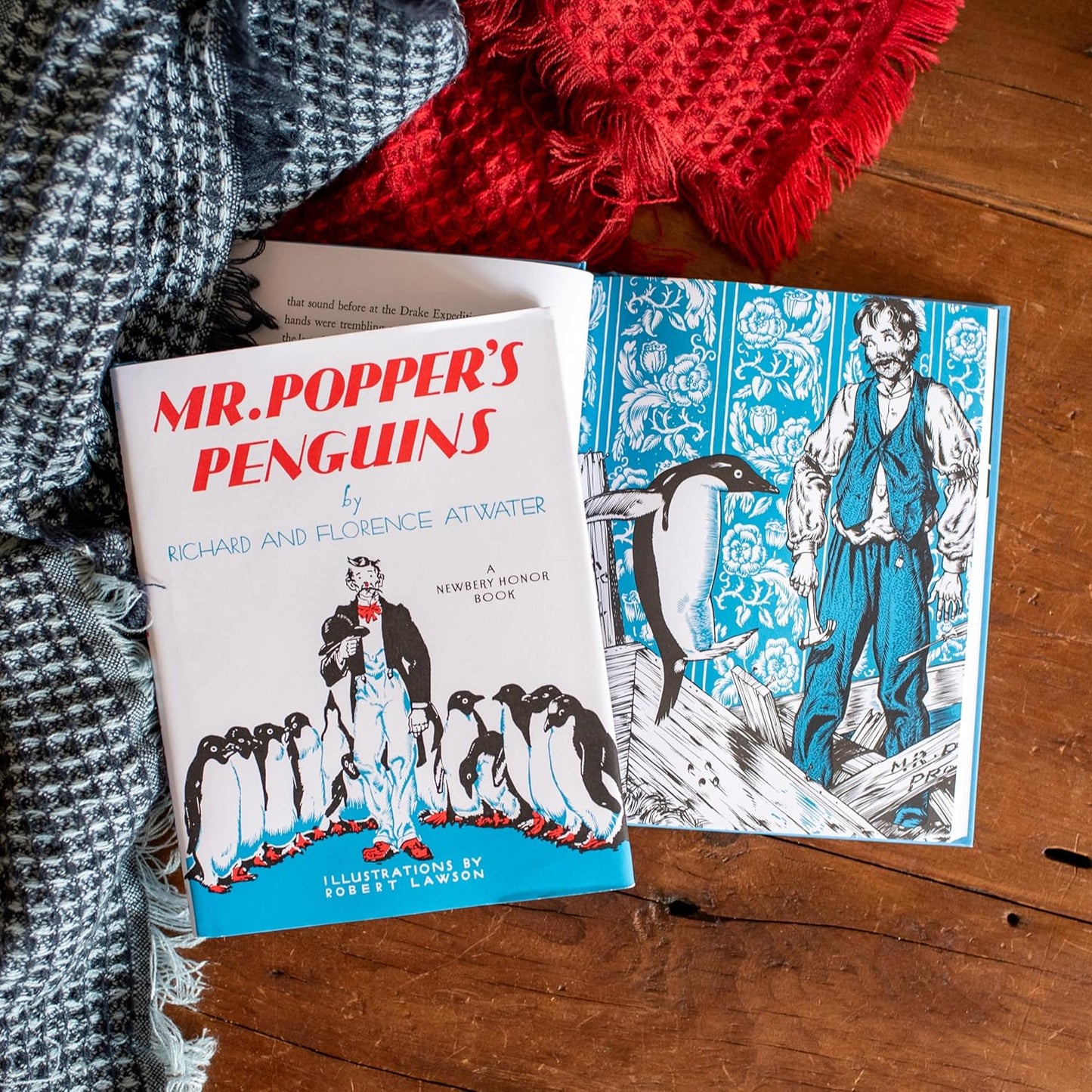 Book titled 'Mr. Popper's Penguins' on a wooden surface with a red and gray textured fabric.
