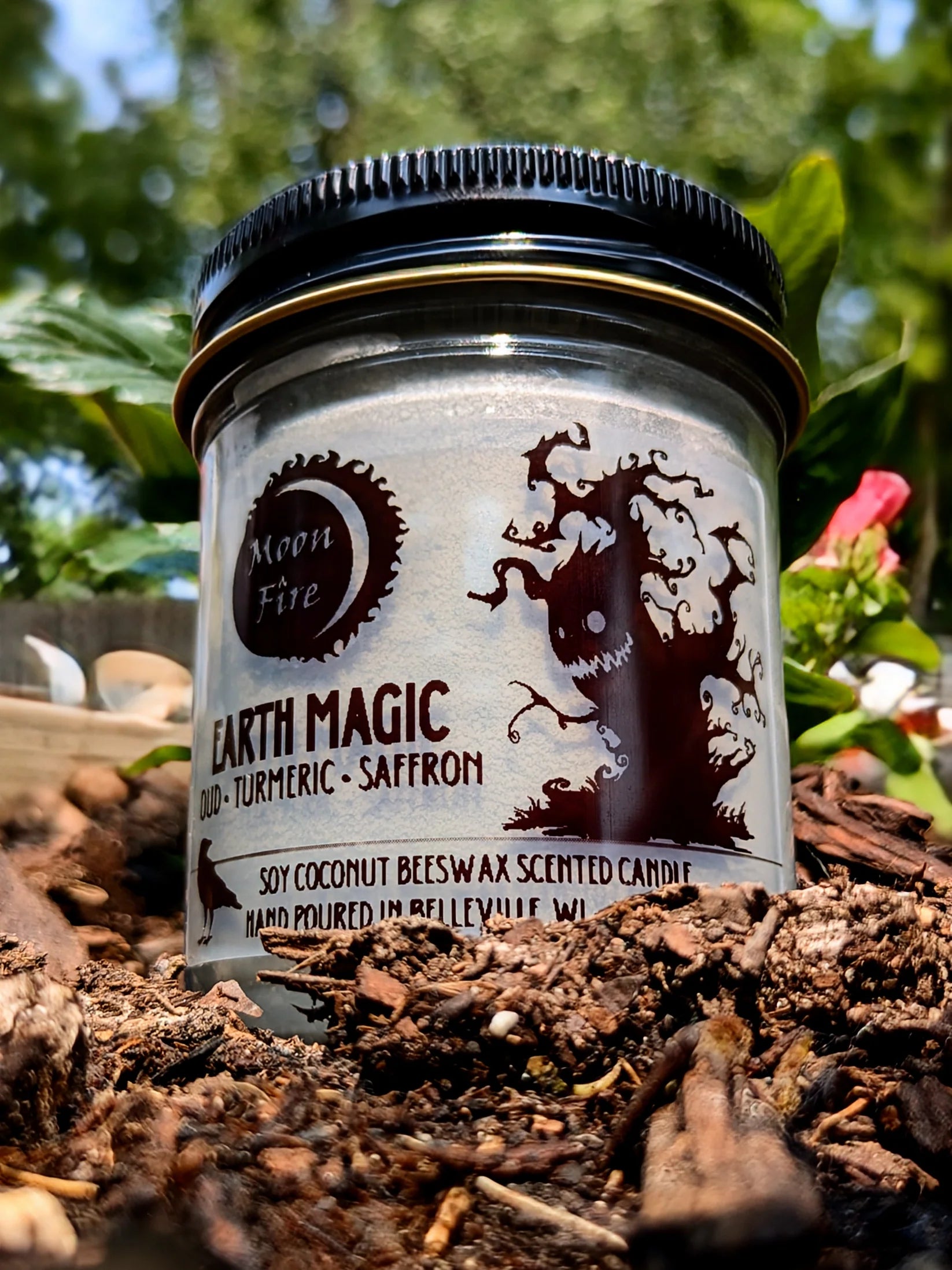 Scented candle jar labeled 'Earth Magic' with nature-themed design on a natural background and Moonfire branding.