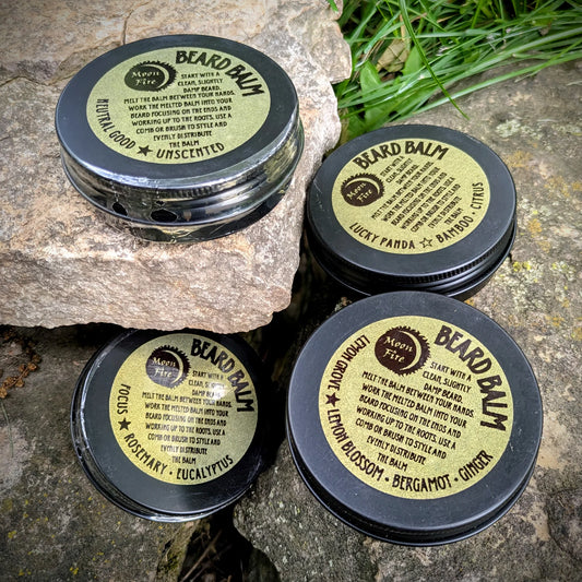 Four containers of beard balm with Moonfire labels on a stone surface.